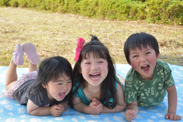 レジャーシートの上でうつ伏せになり笑っている3人の子供たち